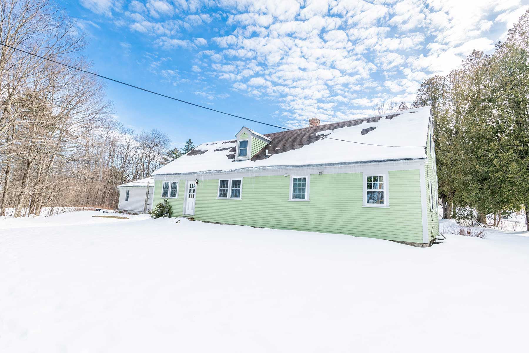 Snow-covered mint-green house in a wooded area under a bright blue sky