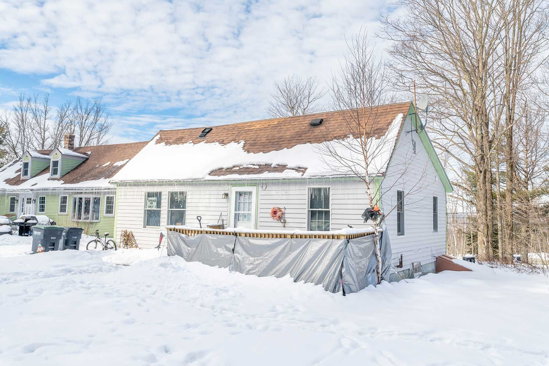 Snow-covered mint-green house in a wooded area under a clear blue sky
