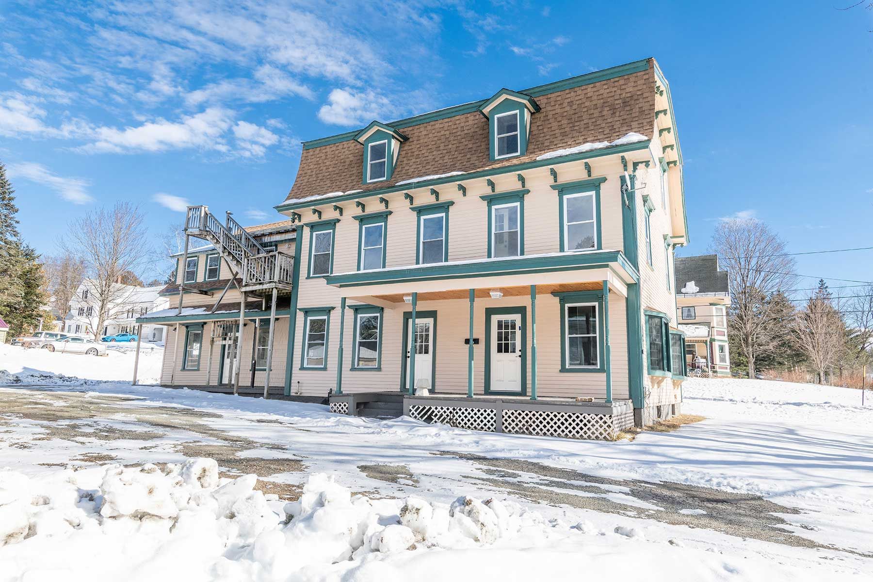 Snow-covered Victorian-style rental home with teal trim and partially renovated porch under a bright winter sky
