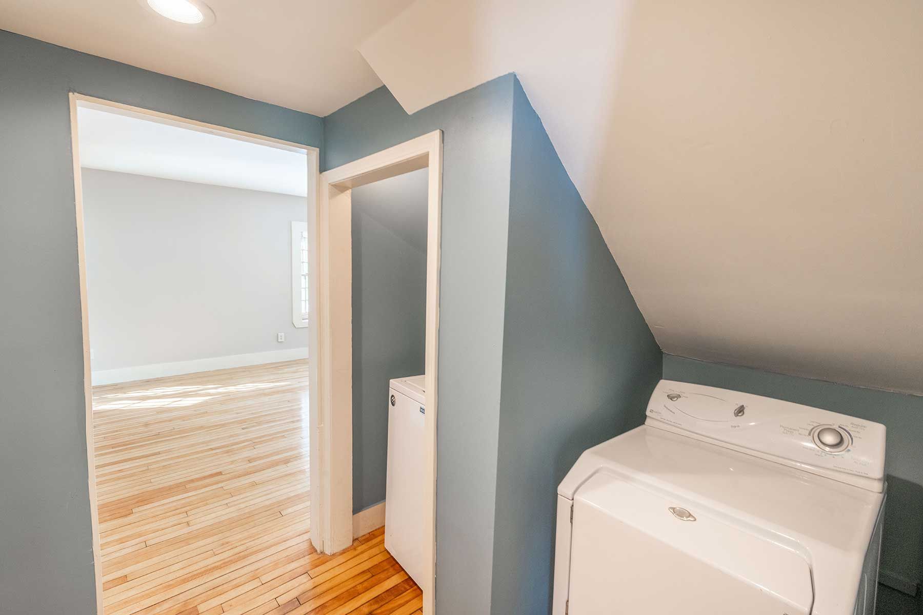 Laundry area with washer next to blue wall and doorway to bright room with wood floors