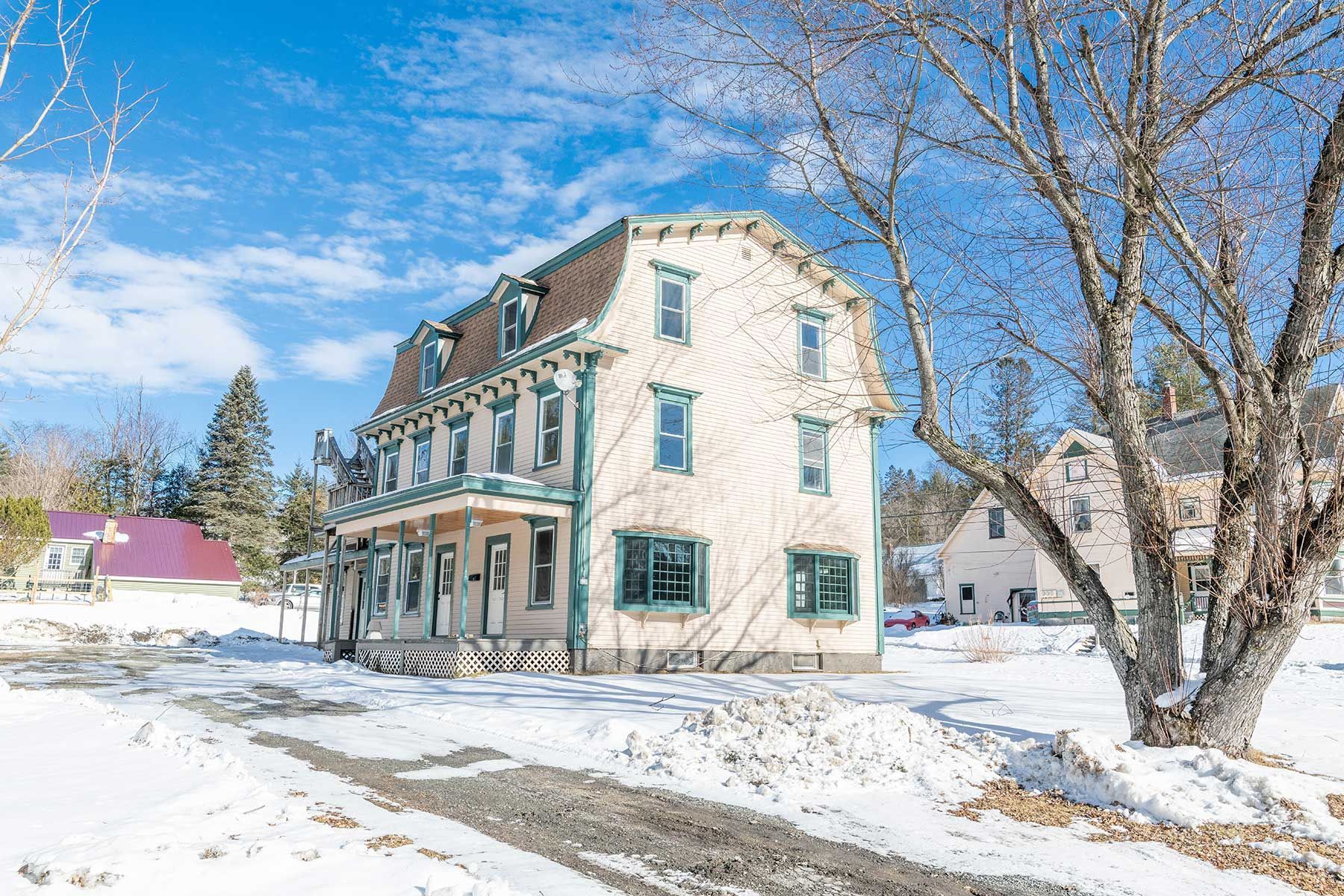 Snow-covered Victorian-style house with turquoise trim next to a leafless tree under a blue sky