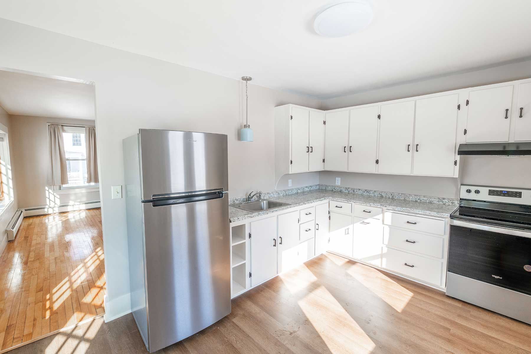 Bright modern rental kitchen with stainless steel refrigerator, white cabinets, and wood floors with natural light