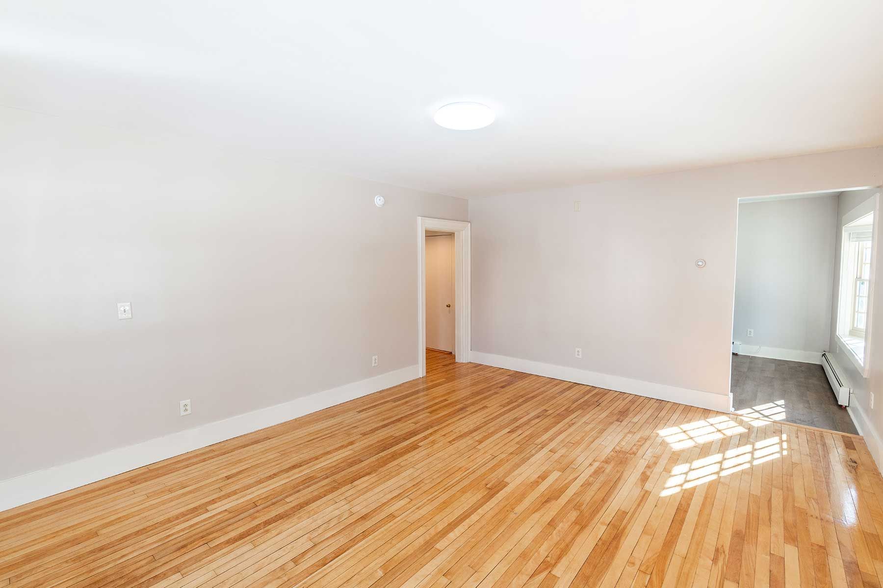 Empty rental room with hardwood floors, beige walls, and natural sunlight from a window