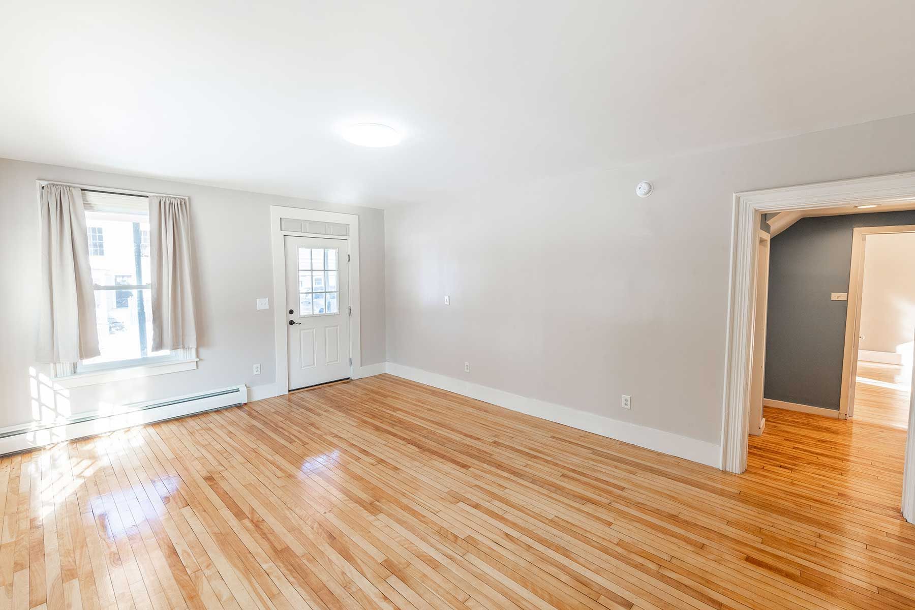 Empty rental room with hardwood floors, beige walls, and doorway leading to a bathroom with natural light