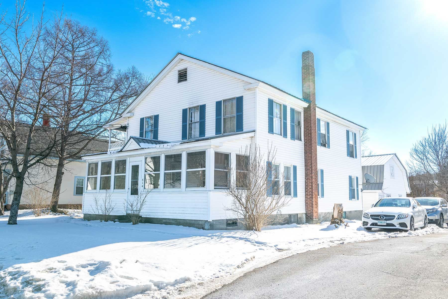 Snow-covered white two-story house with blue shutters on a winter street in Union  Street NH.