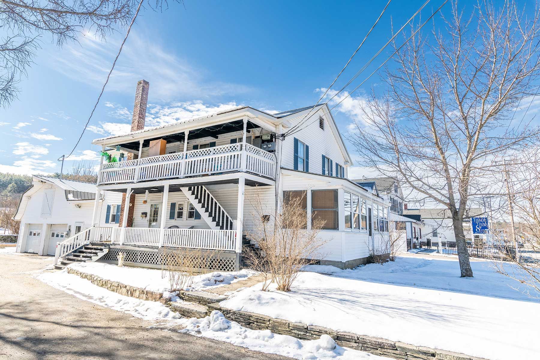 Snow-covered two-story house with white porch and stairs under a bright blue winter sky in Union Street NH.