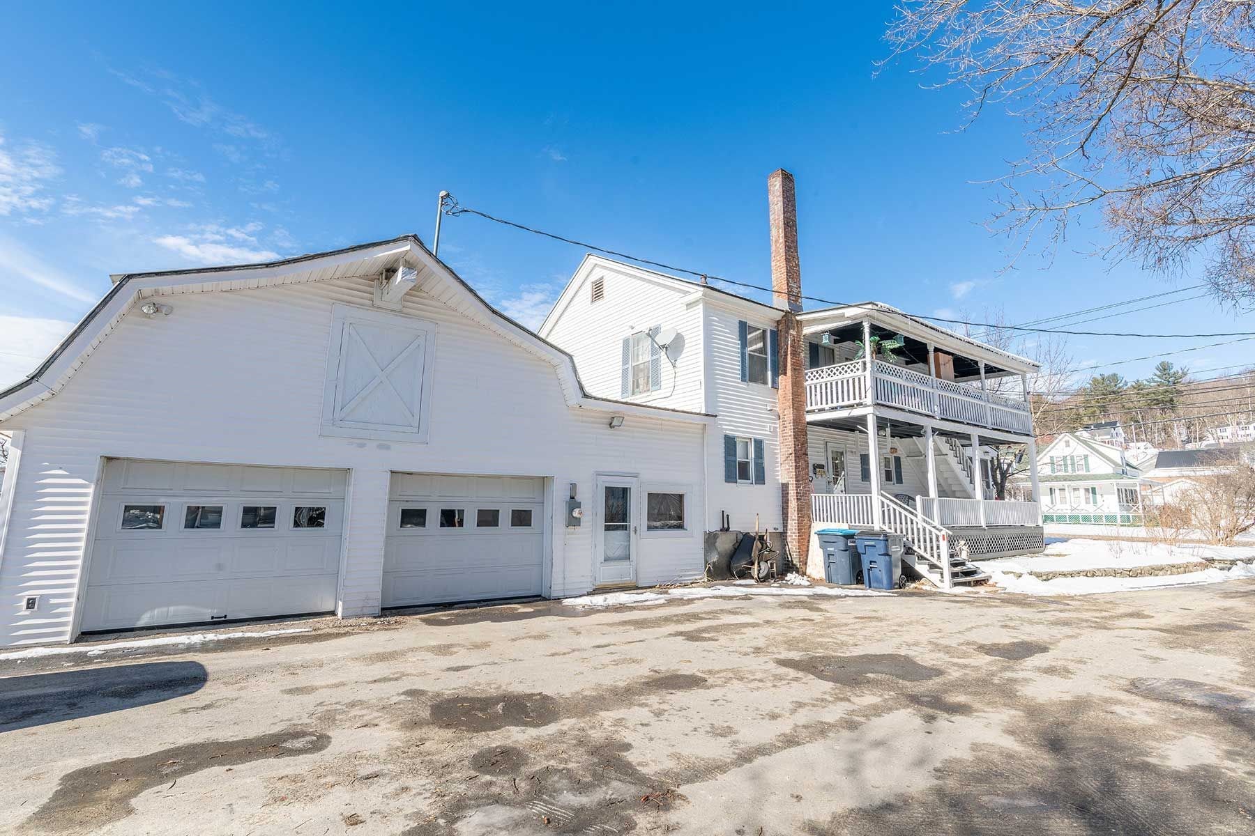 White house with two-car garage and tall chimney beside a partially renovated building on a snowy lot in Union Street NH.
