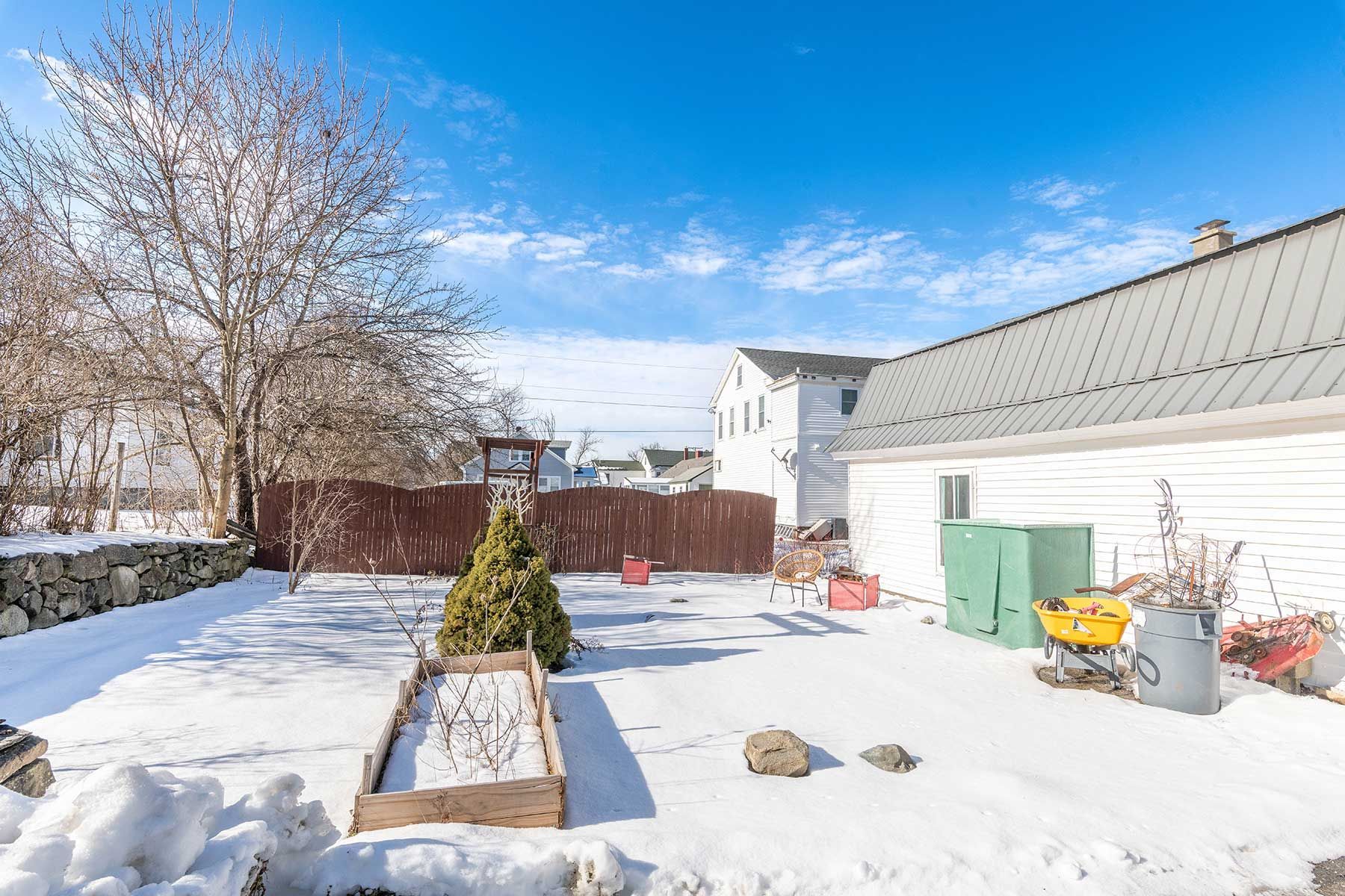 Snow-covered backyard with raised garden bed, tree, fence, and house in Union Street NH.