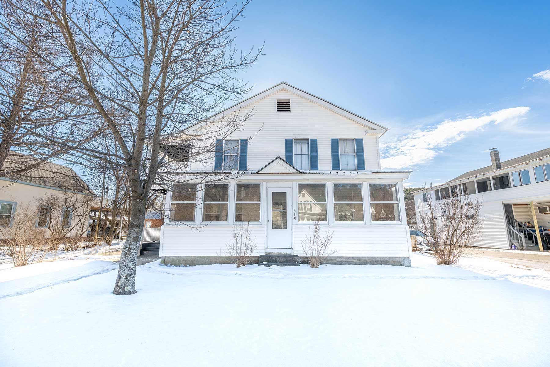 Snowy street with parked cars beside a white two-story building and small white shed under a blue sky in Union NH.