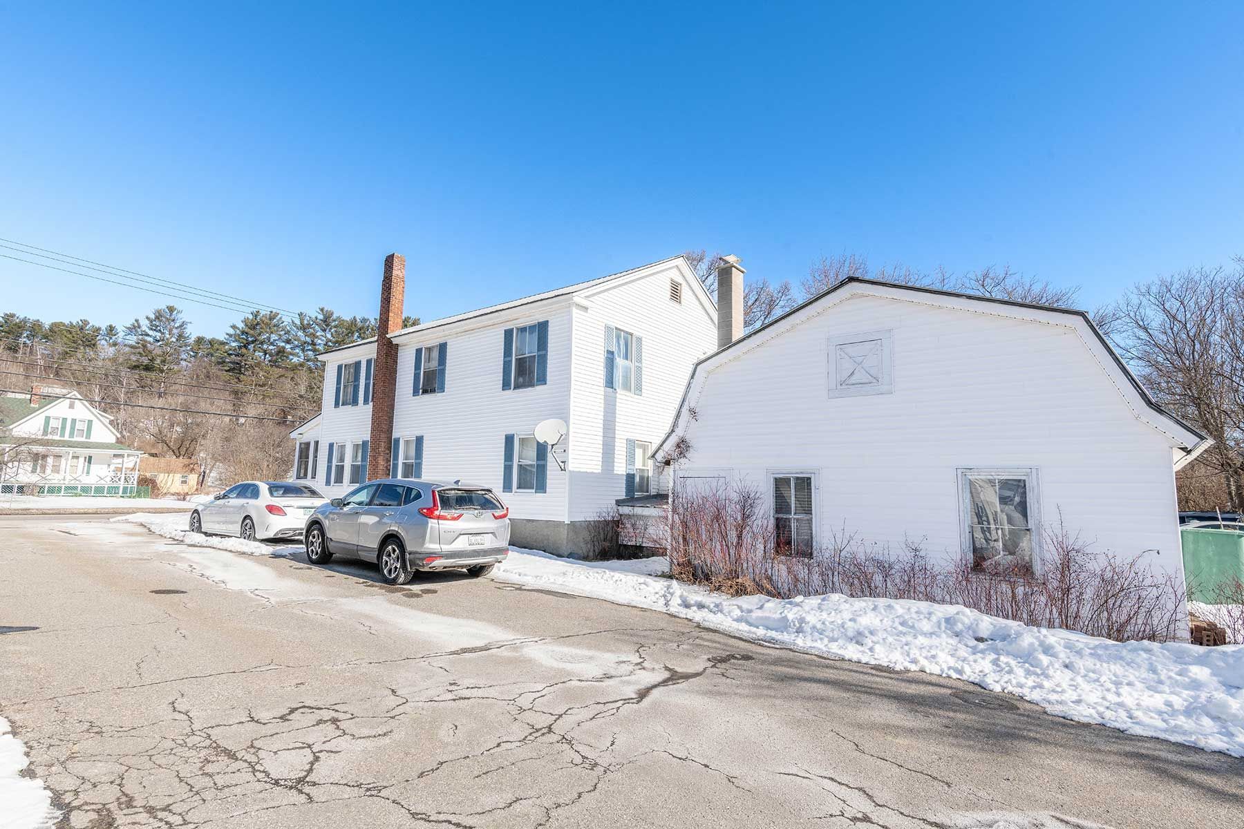 Snowy street with parked cars beside a white two-story building and small white shed under a blue sky in Union Street NH.