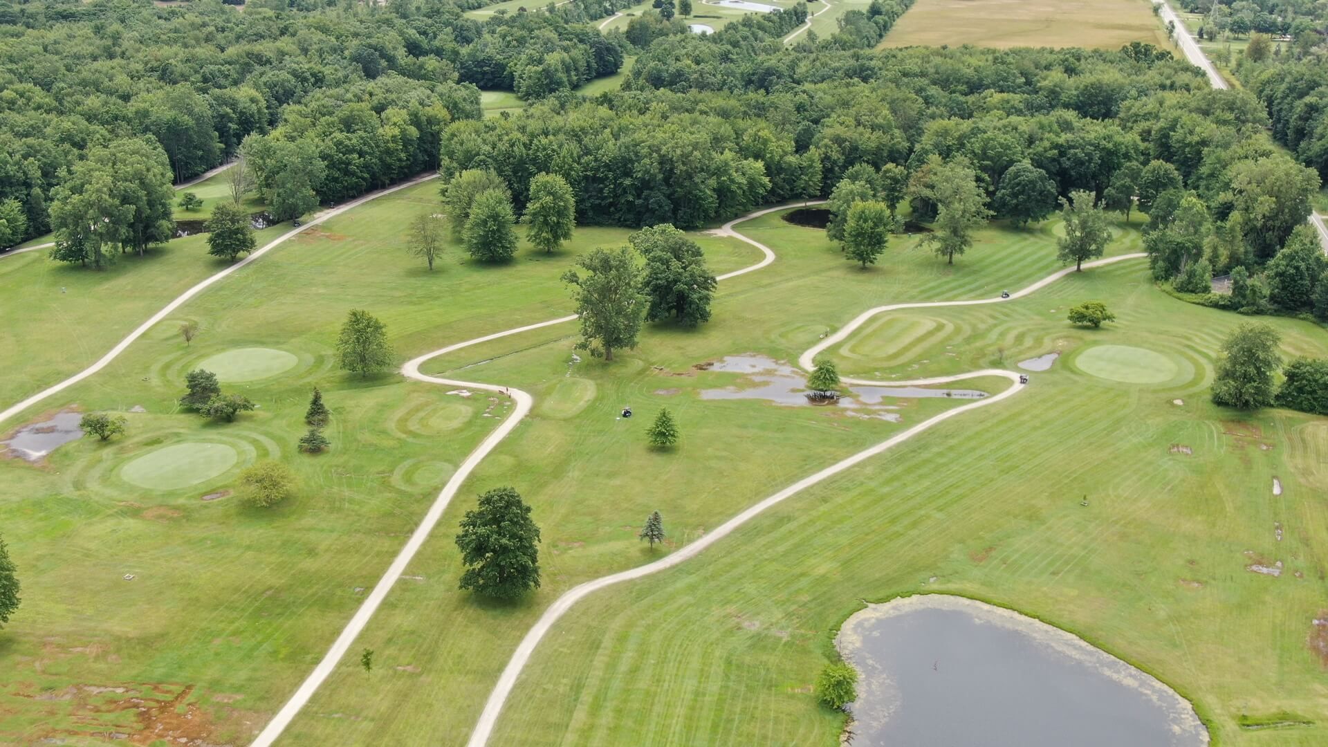 An aerial view of a golf course surrounded by trees and a pond.