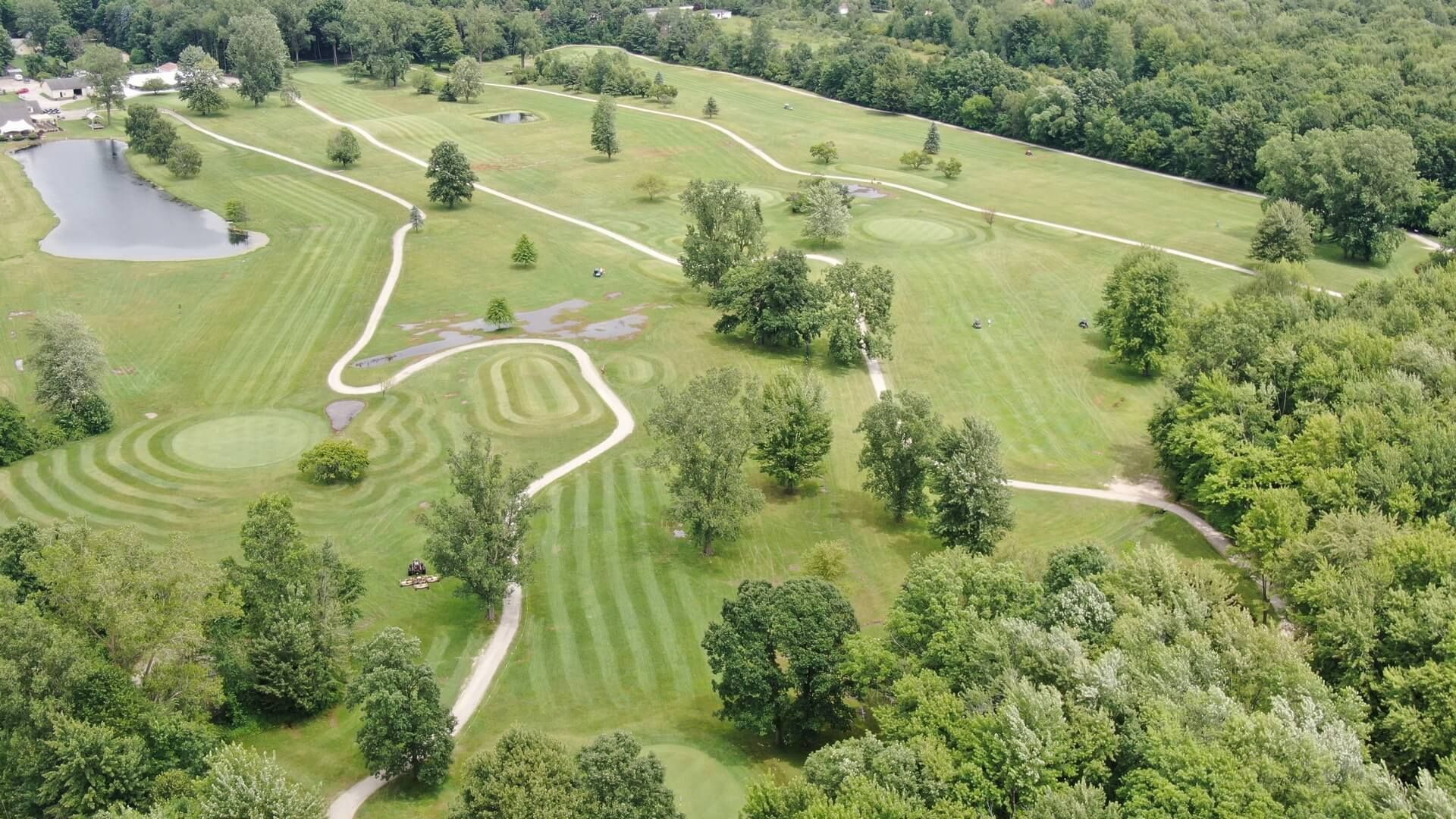 An aerial view of a golf course surrounded by trees and a pond.