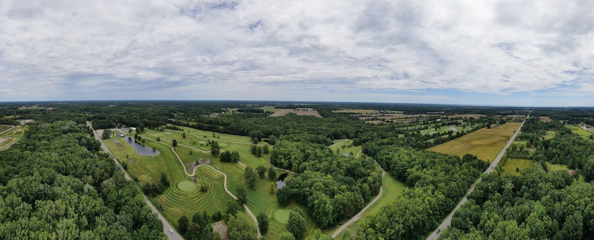 An aerial view of a golf course surrounded by trees and a road.