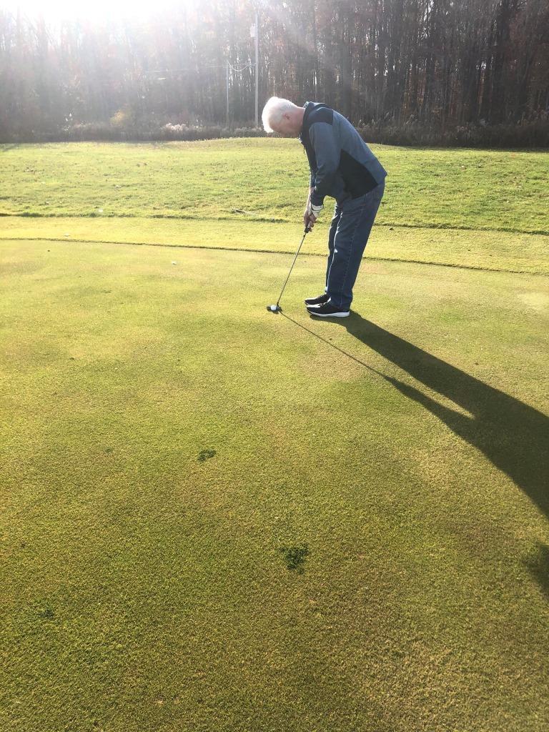 A man is bending over to putt a golf ball.