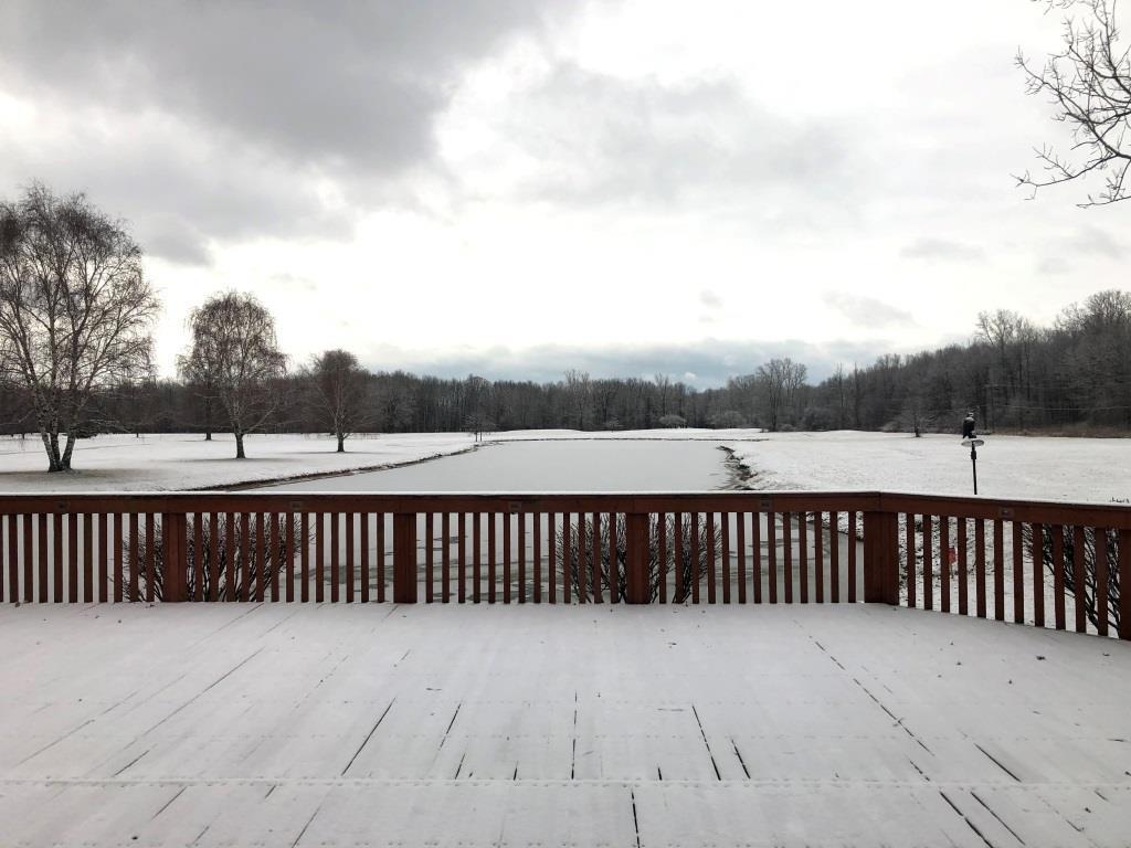 A snowy deck with a fence and trees in the background.