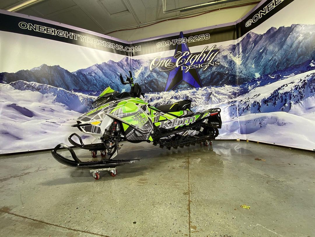 A snowmobile is parked in a garage in front of a wall with mountains on it.