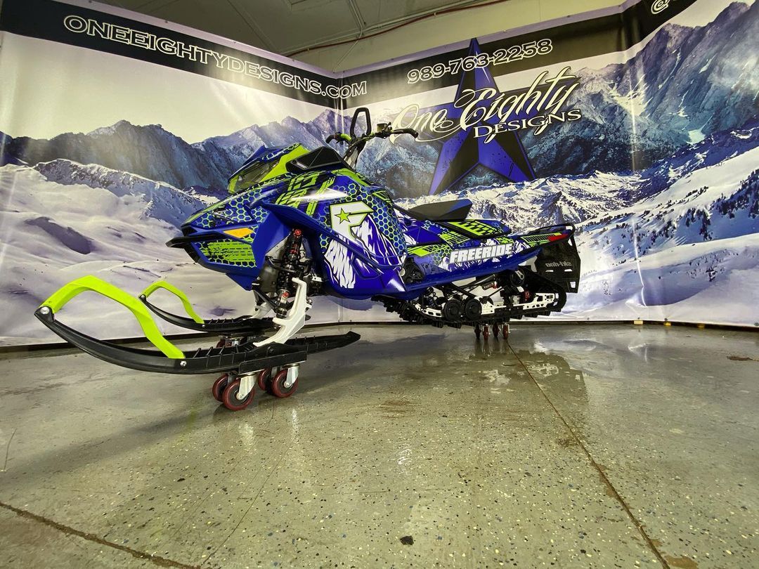 A blue and yellow snowmobile is parked in a garage.