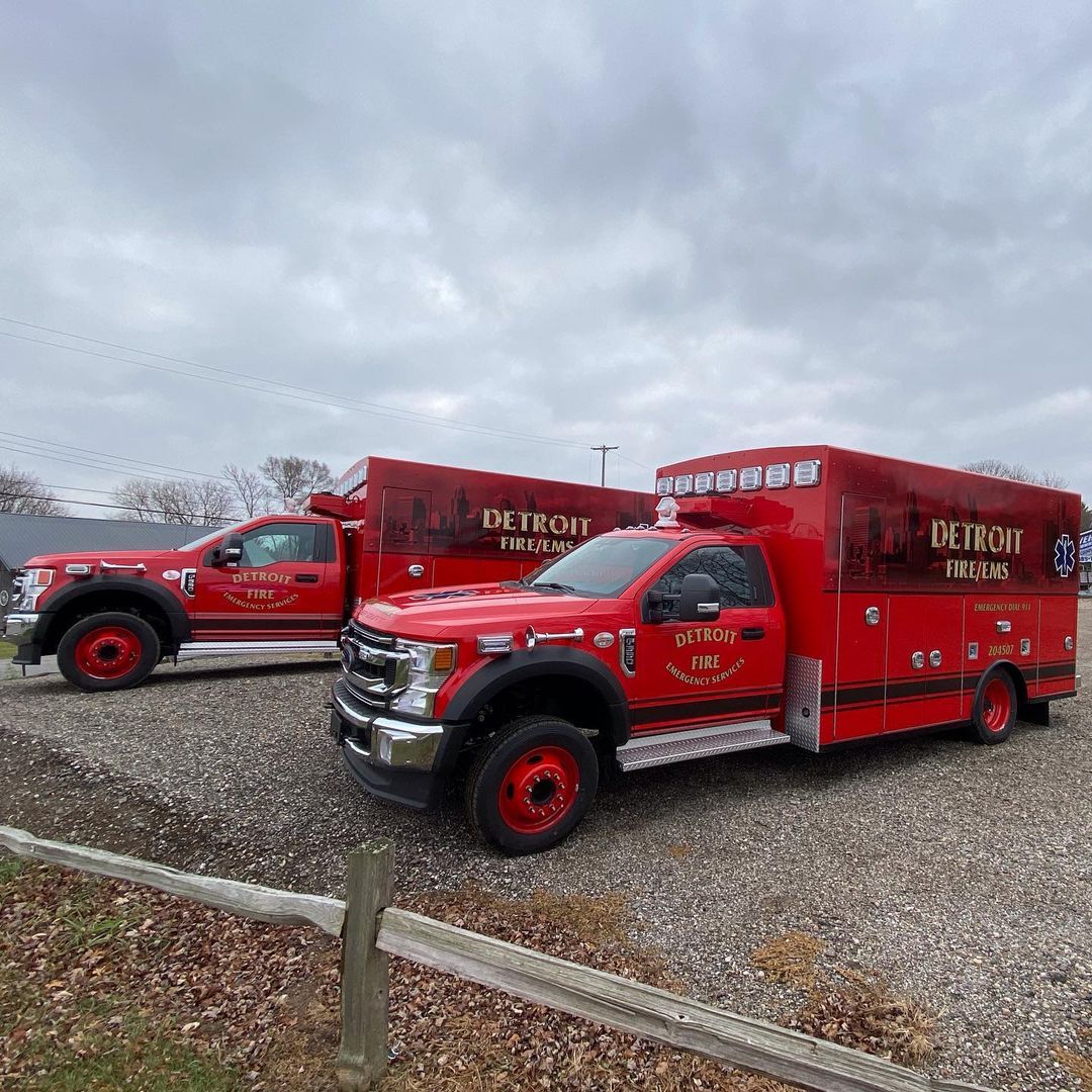 Two red fire trucks are parked next to each other in a gravel lot.