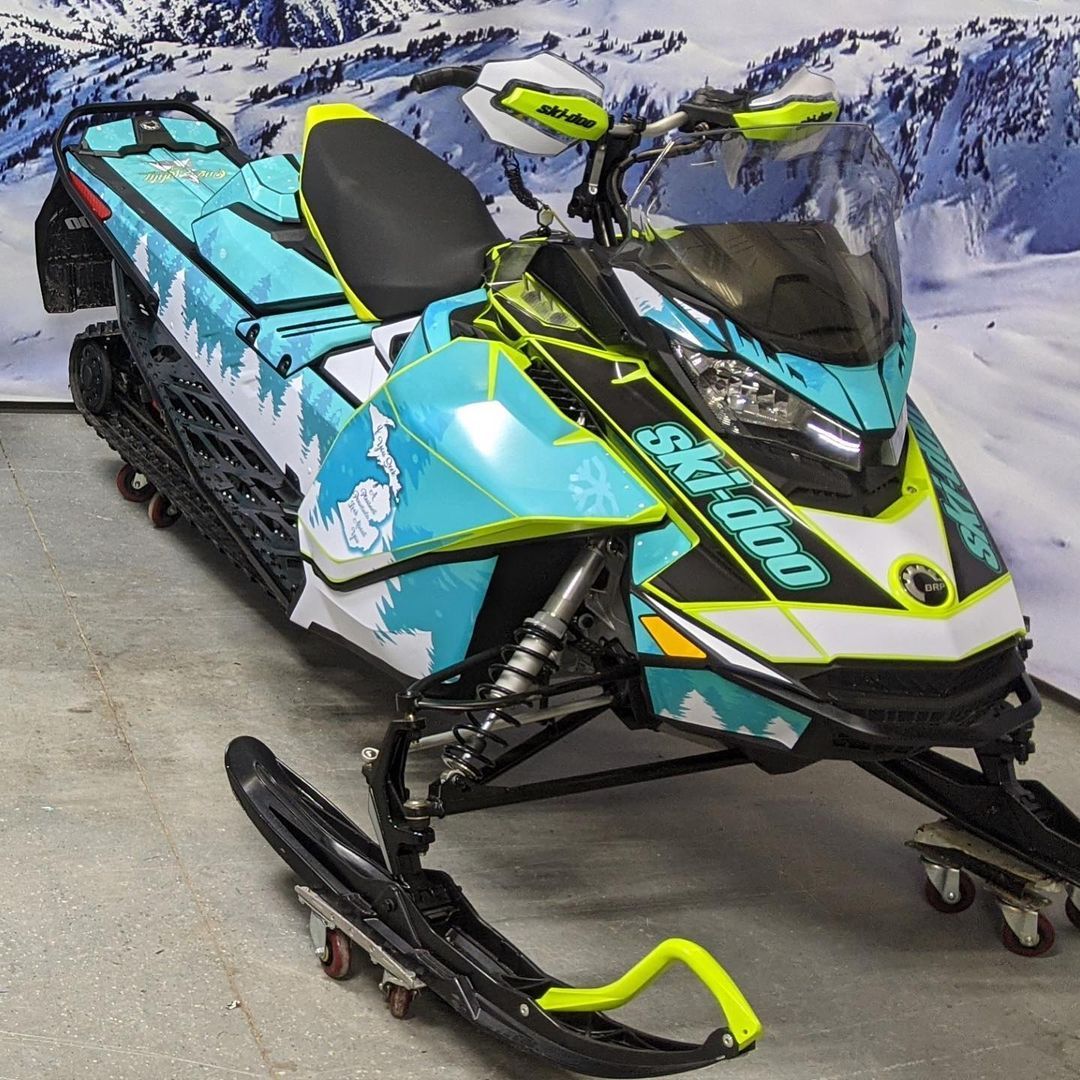 A blue and yellow snowmobile is parked in front of a snowy mountain.