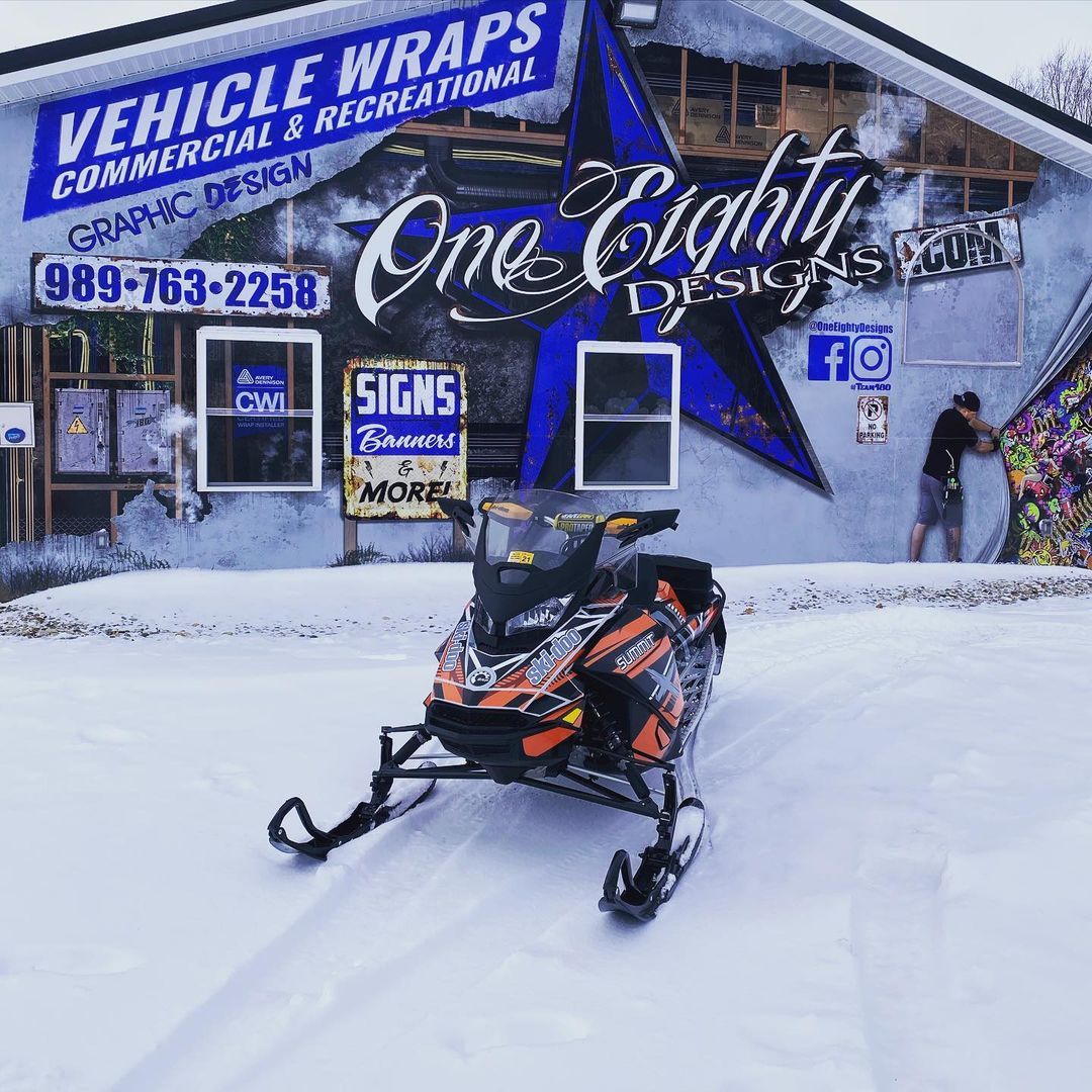 A snowmobile is parked in front of a building that says vehicle wraps