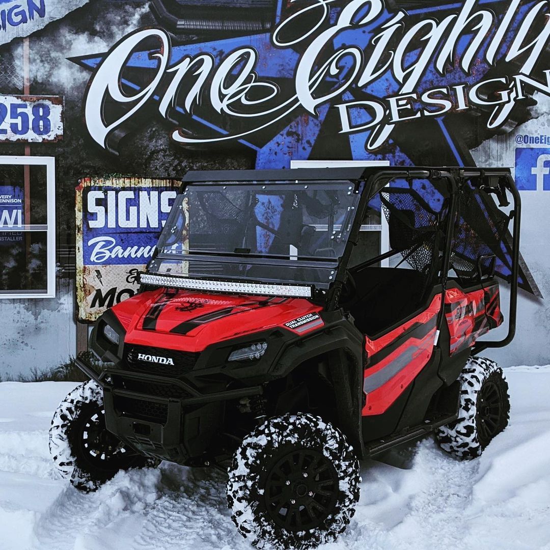 A red atv is parked in the snow in front of a sign that says one eighty design