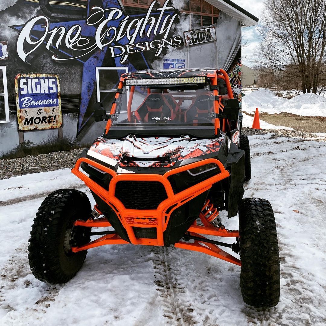 An atv is parked in the snow in front of a building that says one eighty designs