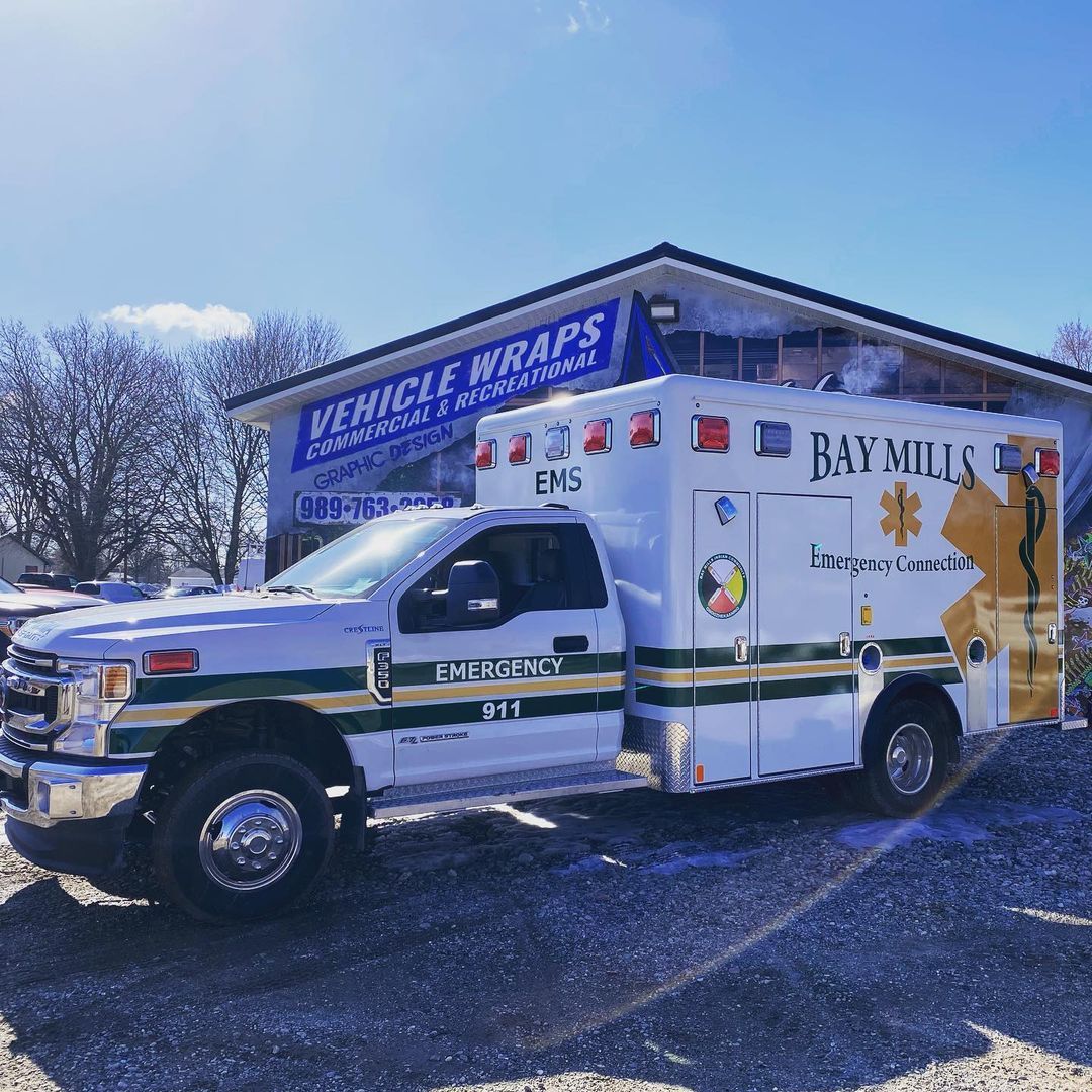 An ambulance is parked in front of a building that says vehicle wraps