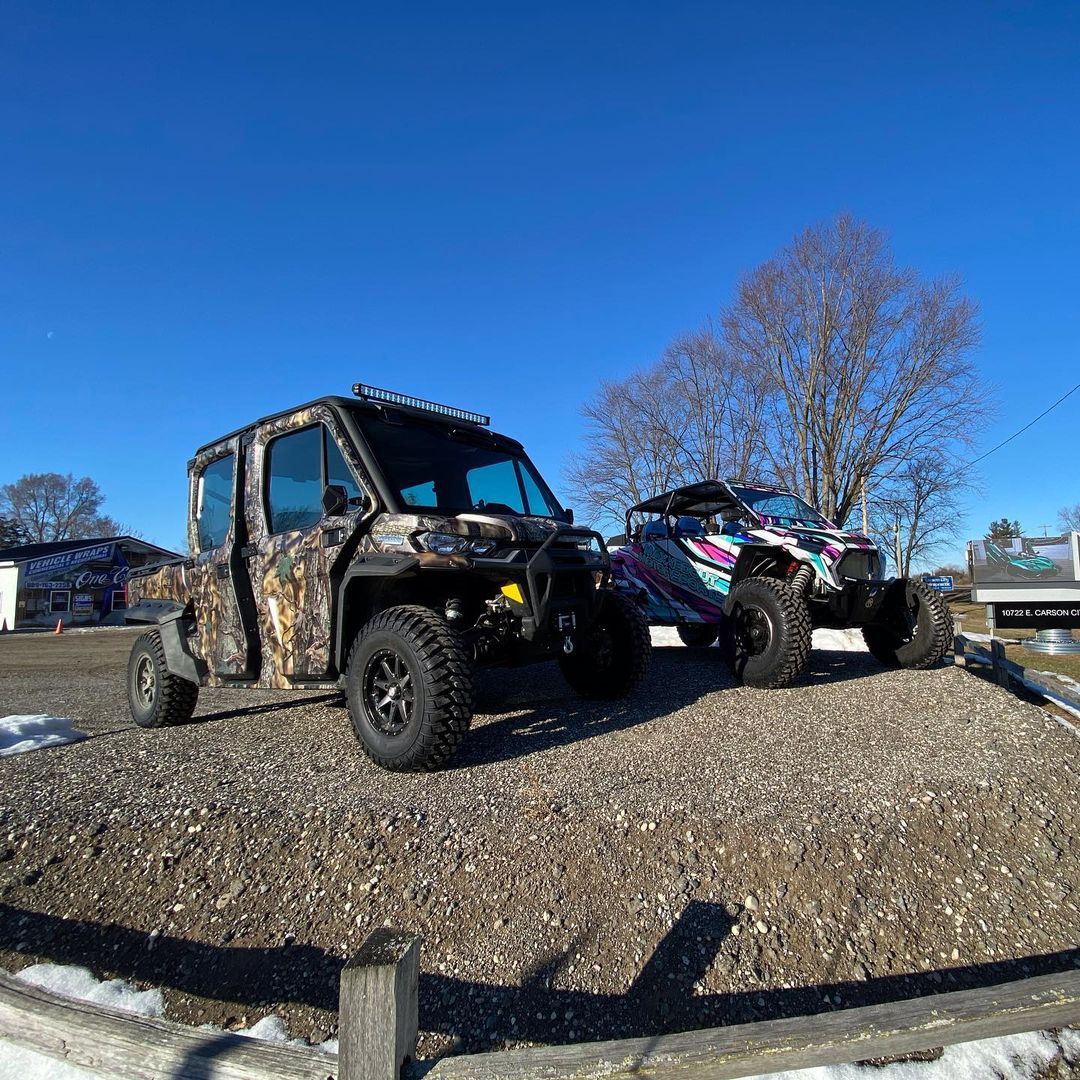Two atvs are parked next to each other in a gravel lot.