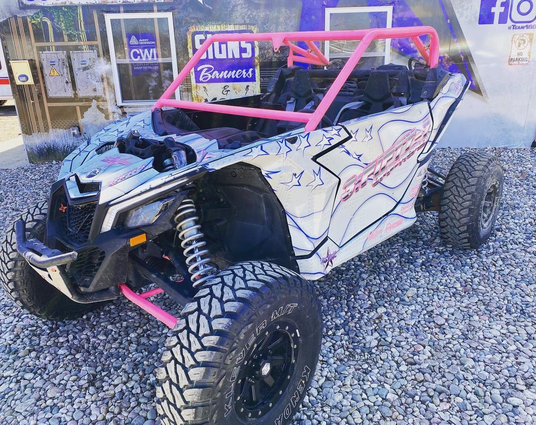 A white and pink atv is parked on gravel in front of a building.