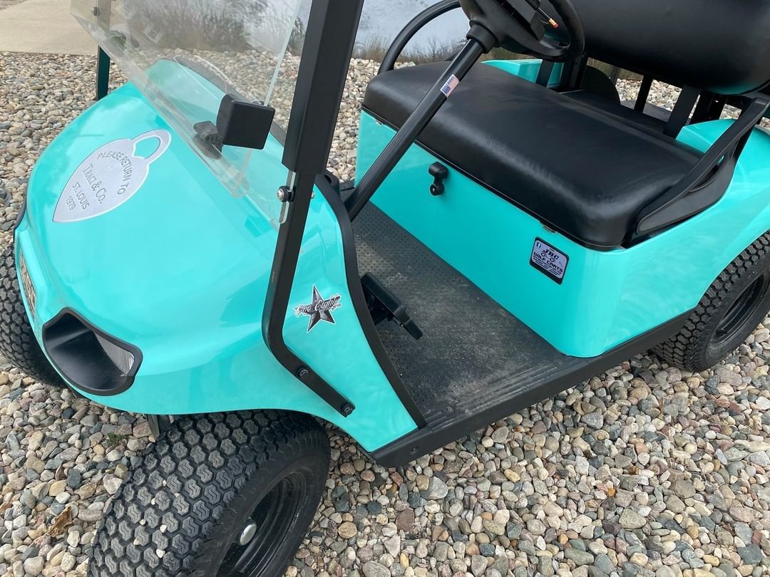 A blue golf cart is parked on a gravel road.