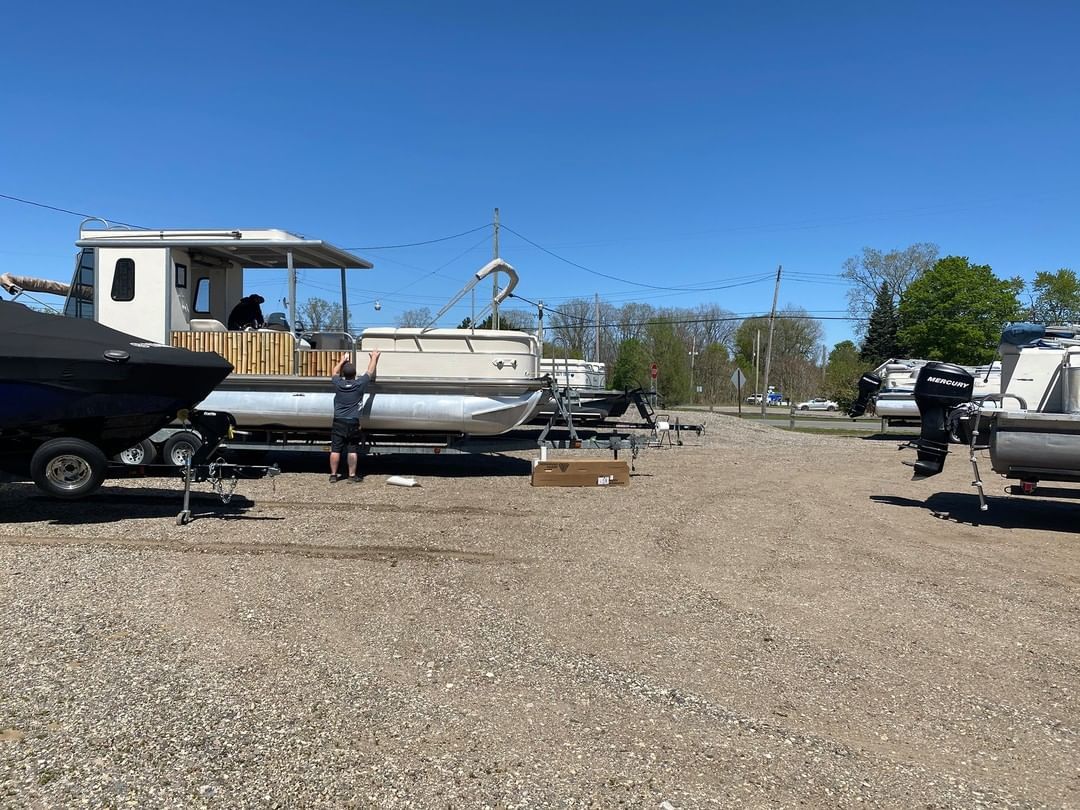 A row of pontoon boats are parked in a gravel lot.