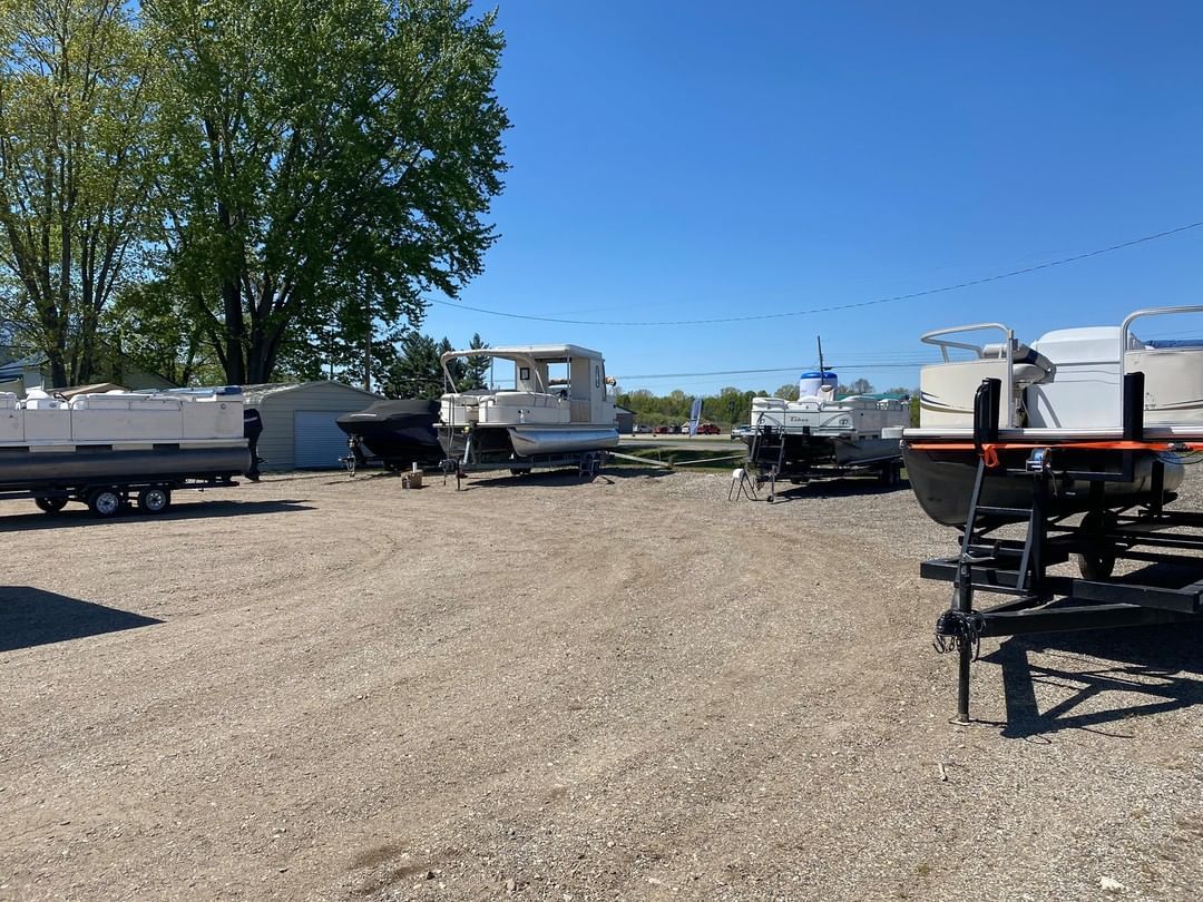 A row of boats are parked in a gravel lot.