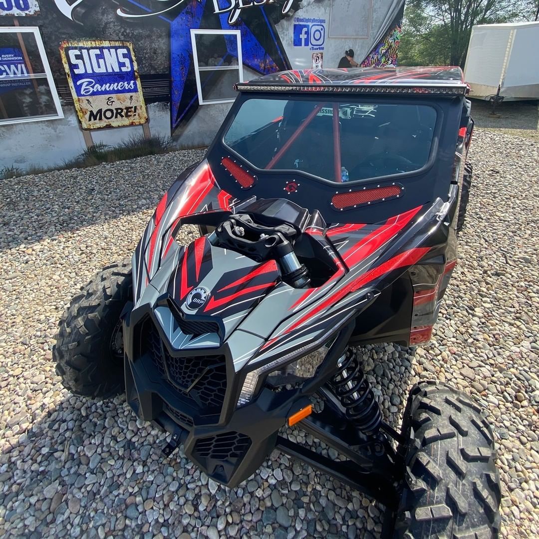 A red and black atv is parked in a gravel lot.