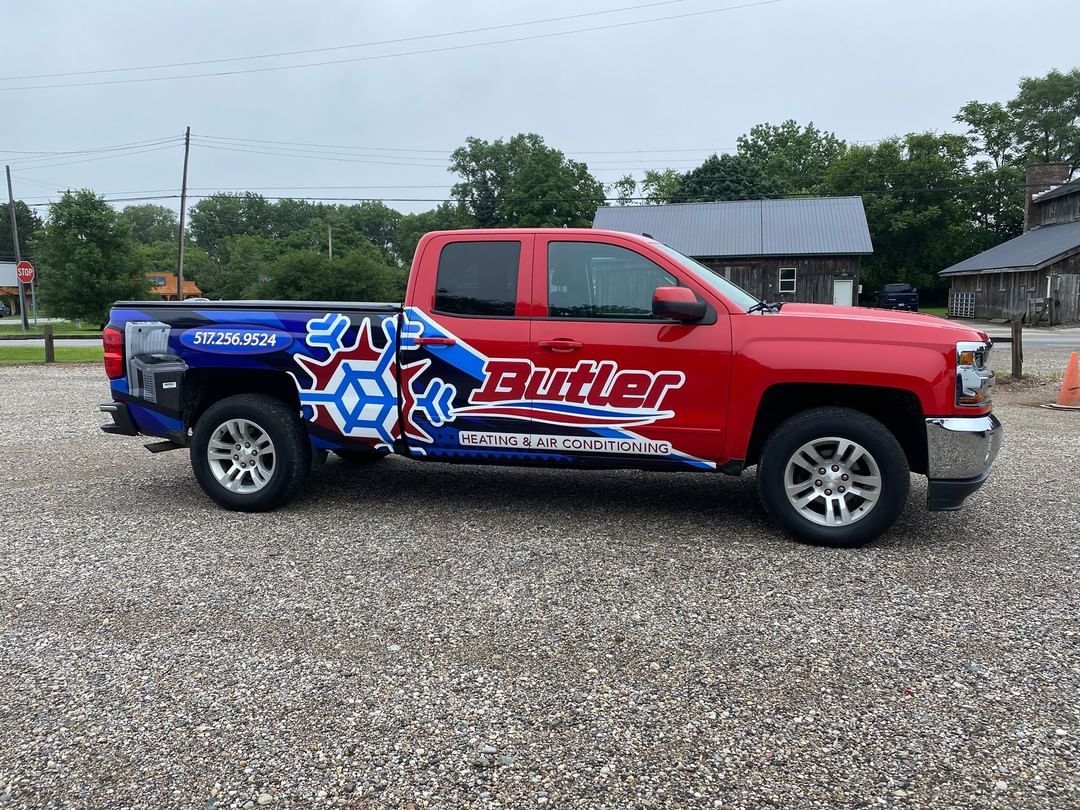 A red and blue pickup truck is parked in a gravel lot.