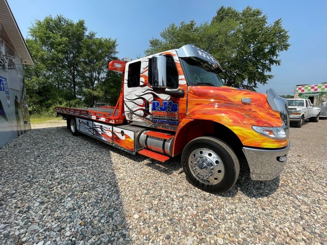 A red tow truck is parked in a gravel lot.