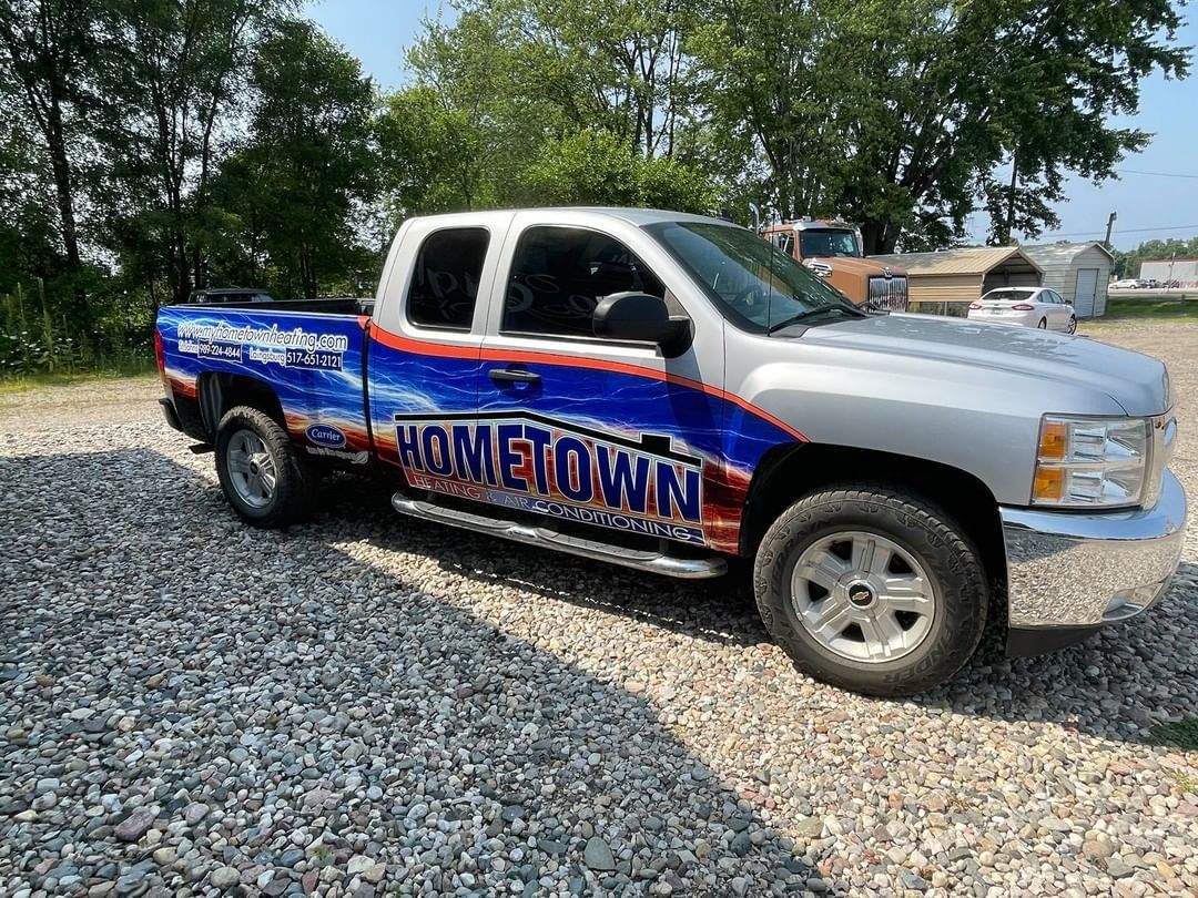 A truck with a wrap on it is parked in a gravel lot.