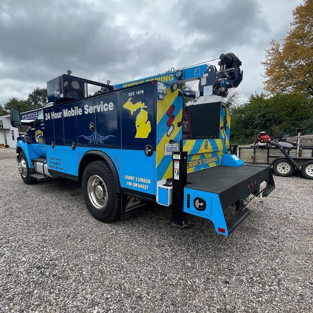 A blue and yellow tow truck is parked in a gravel lot.