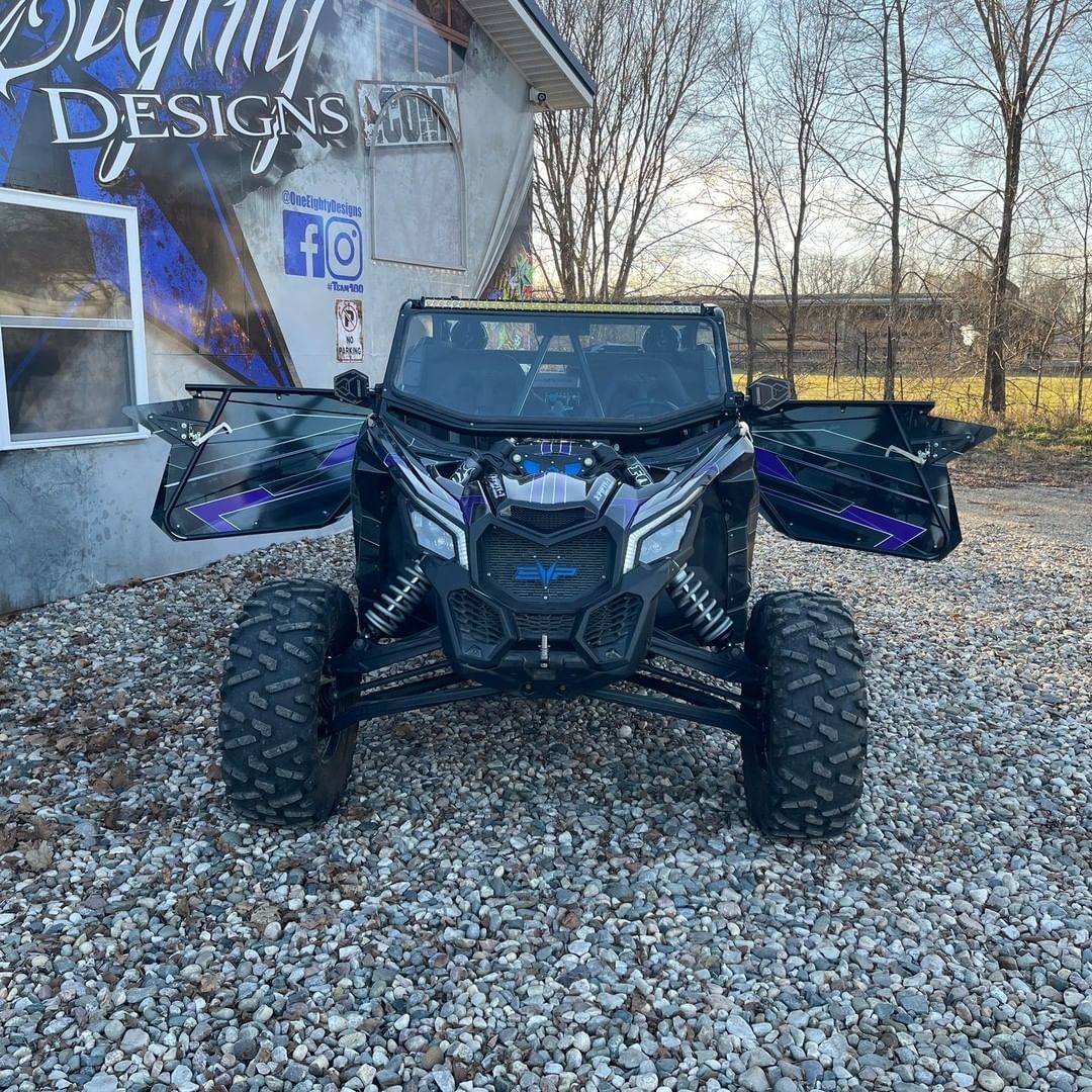 A black atv with its doors open is parked in a gravel lot in front of a building.