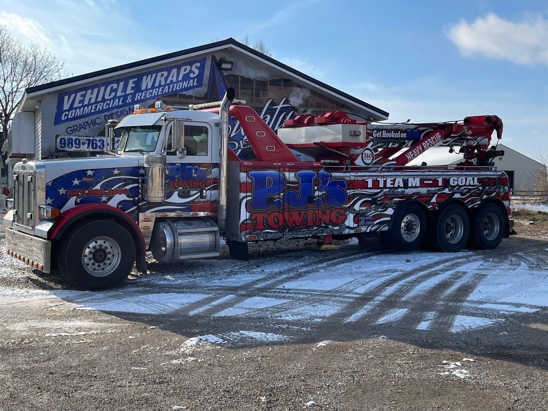 A tow truck is parked in front of a building that says vehicle wraps.