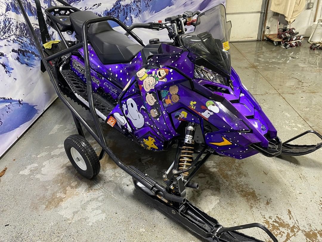 A purple snowmobile is parked in a garage.