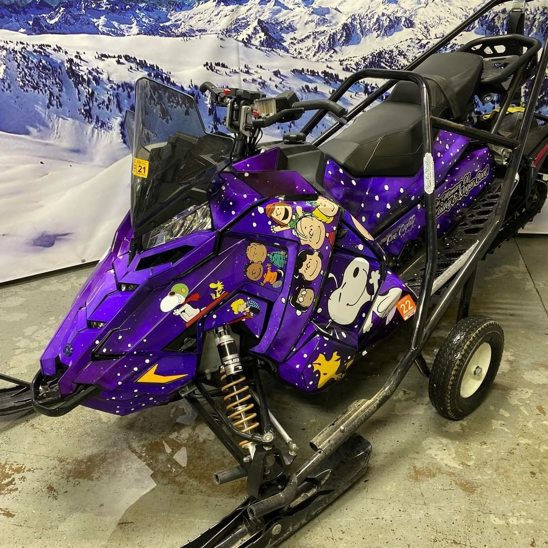 A purple snowmobile with stickers on it is parked in a garage.