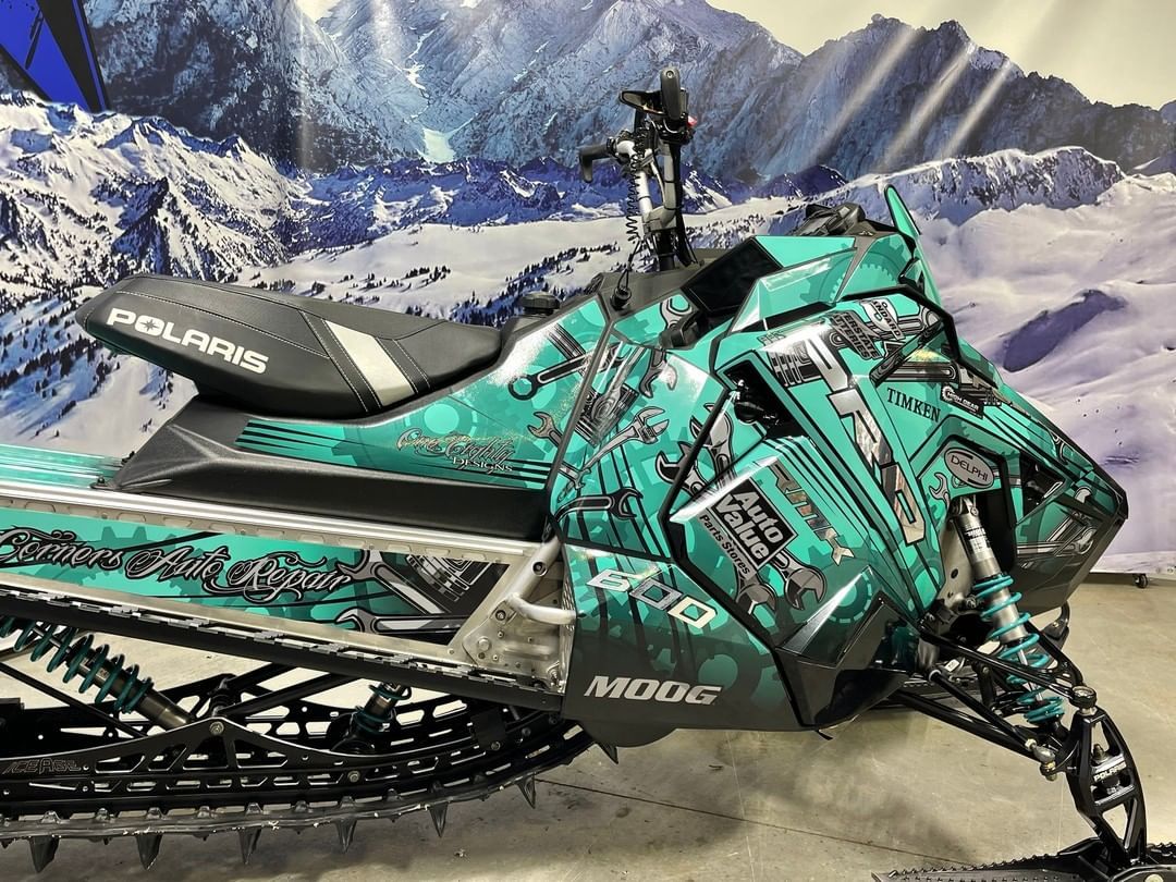 A green snowmobile is parked in front of a snowy mountain.