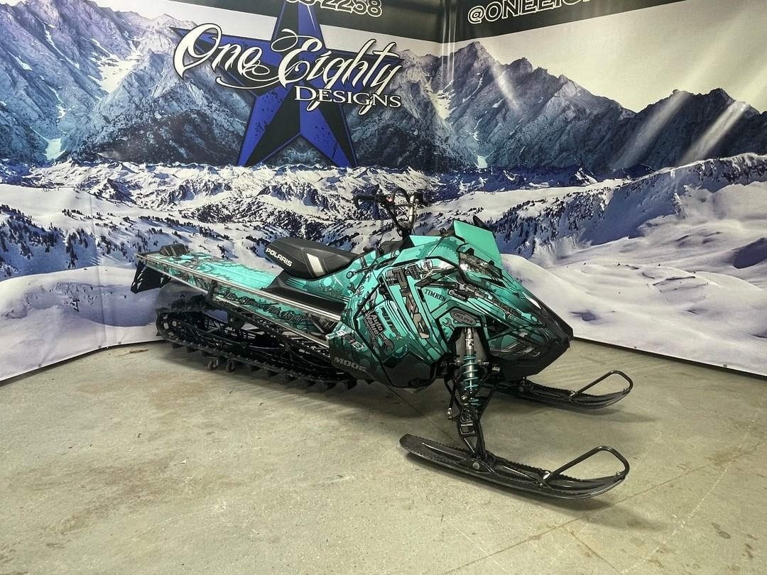 A green snowmobile is parked in front of a snowy mountain.