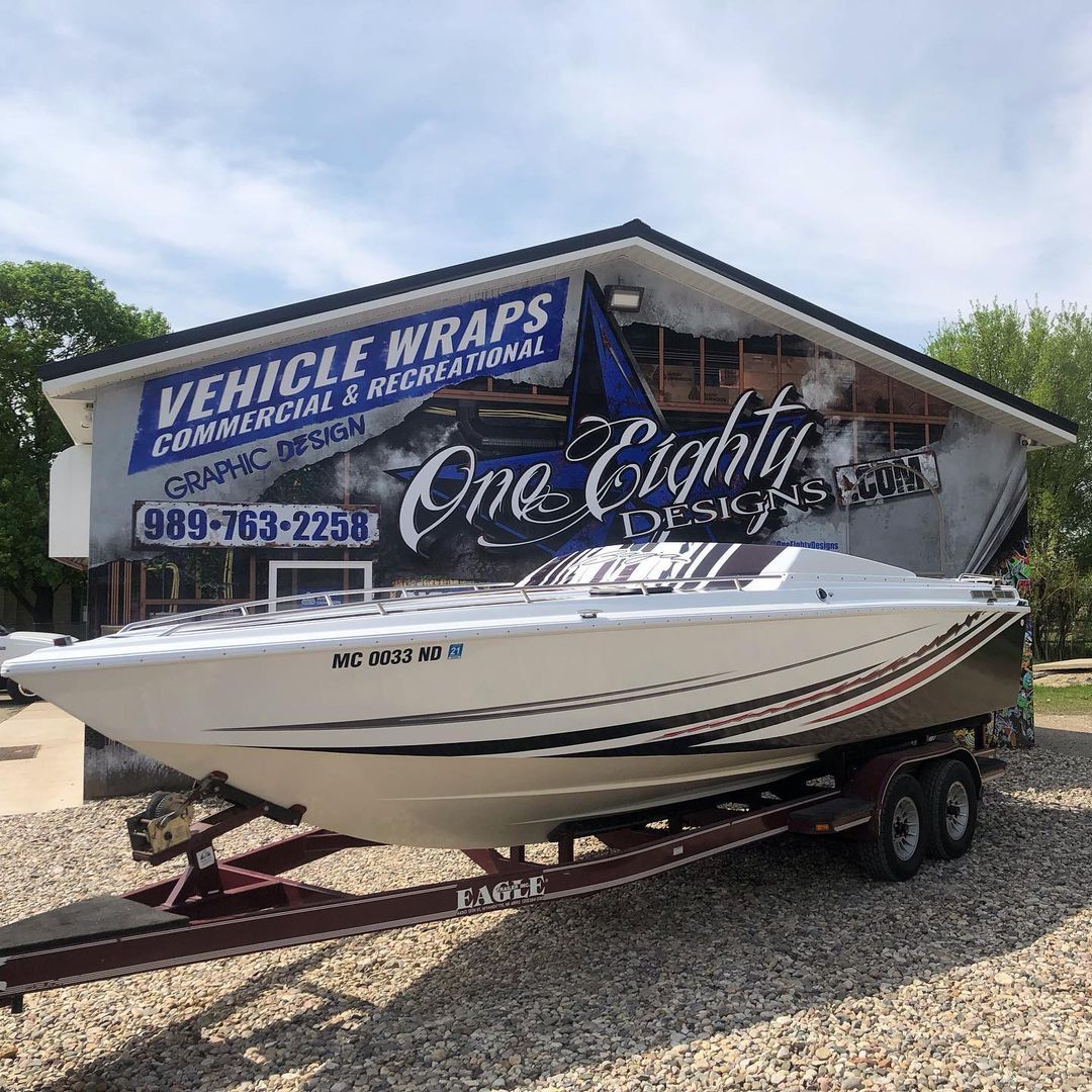 A boat is parked in front of a building that says vehicle wraps.