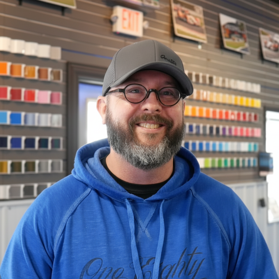 A man wearing a hat and glasses is smiling in front of an exit sign