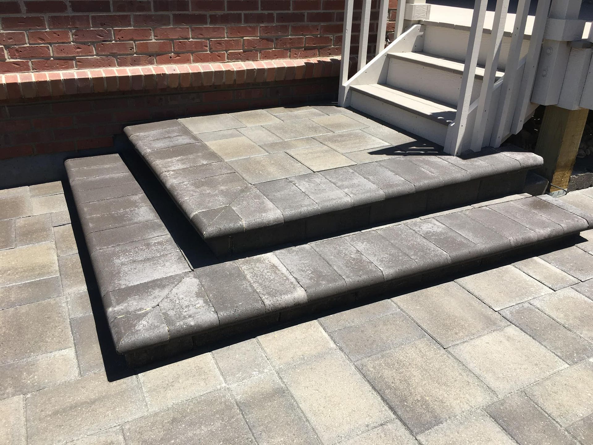 Stone steps leading up to a white staircase and brick wall. The steps are made of dark gray pavers.