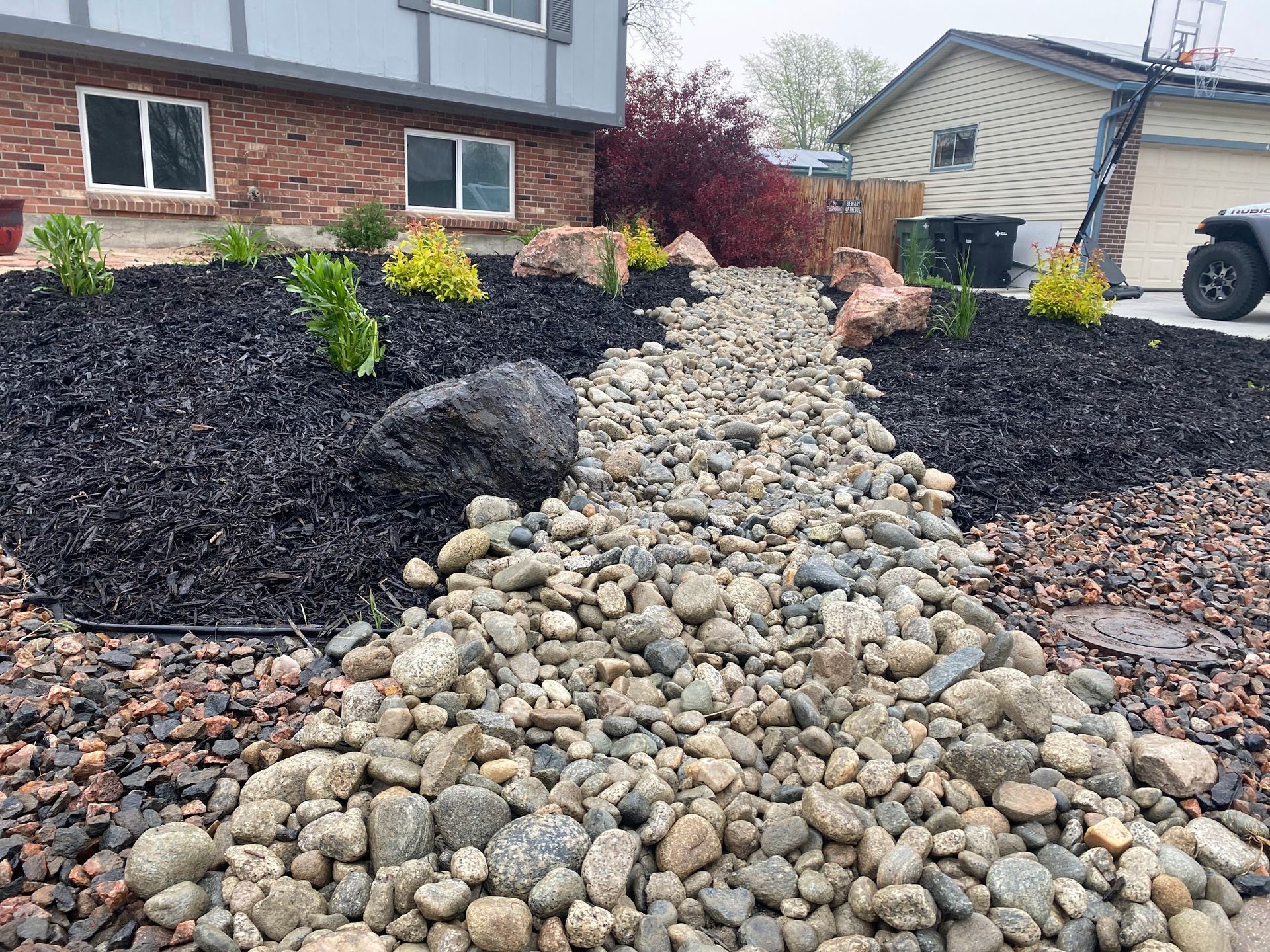 A residential landscaping project featuring a dry creek bed made of river rock and mulch beds with small plants.
