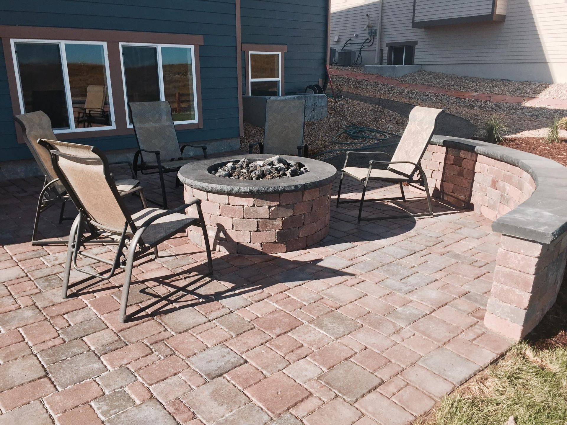 A brick patio with a built-in fire pit and seating. A low brick wall curves along the right side.