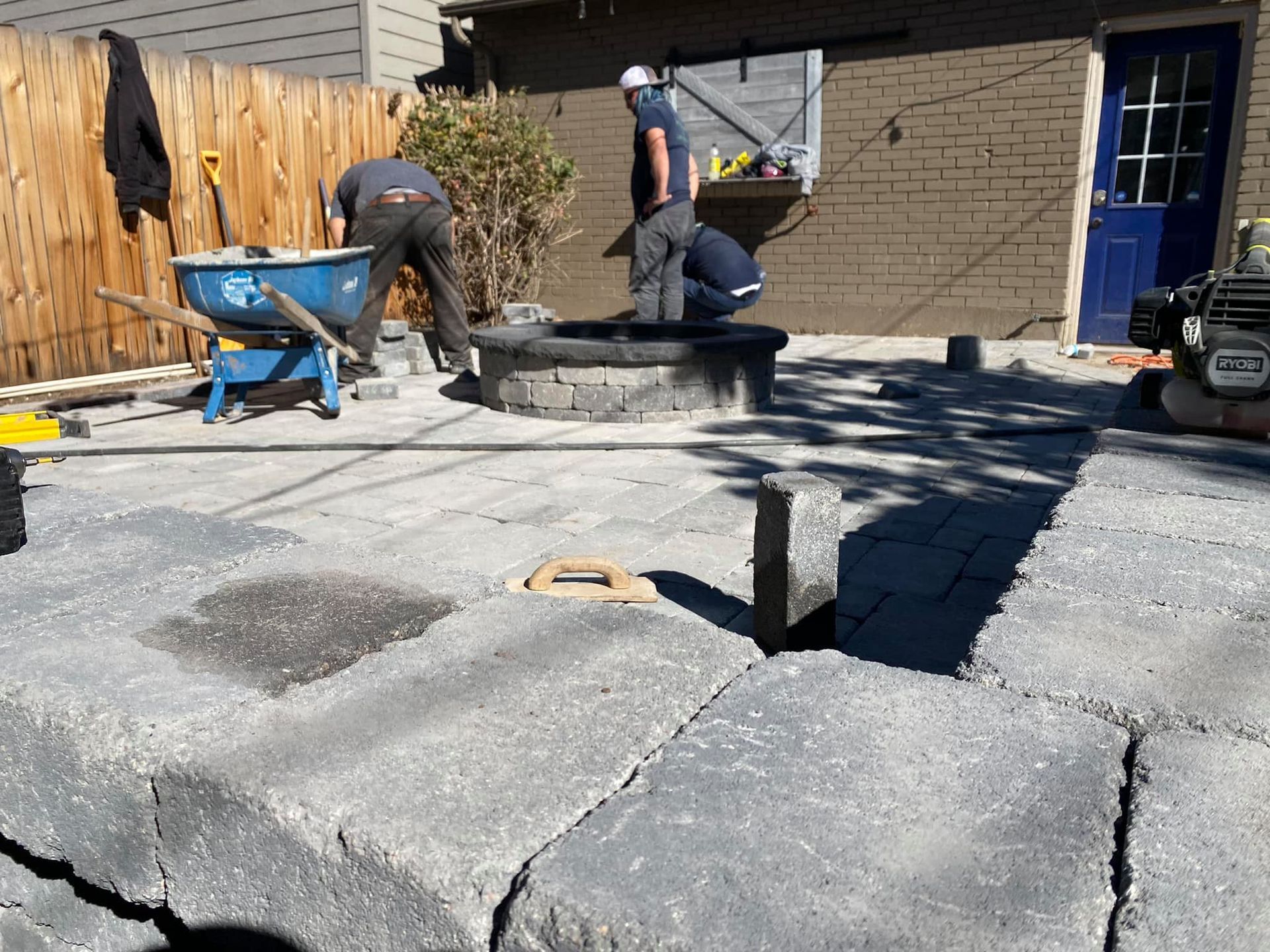 Construction workers building a patio with gray pavers and a fire pit.