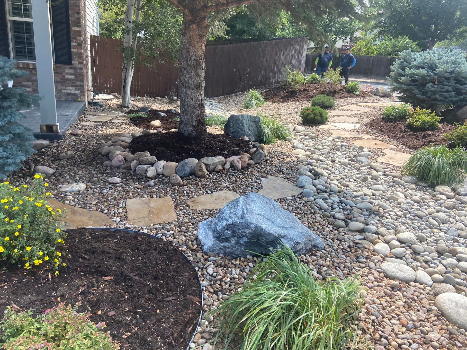 A landscaped front yard with a rock garden, stepping stones, and a tree trunk surrounded by rocks.